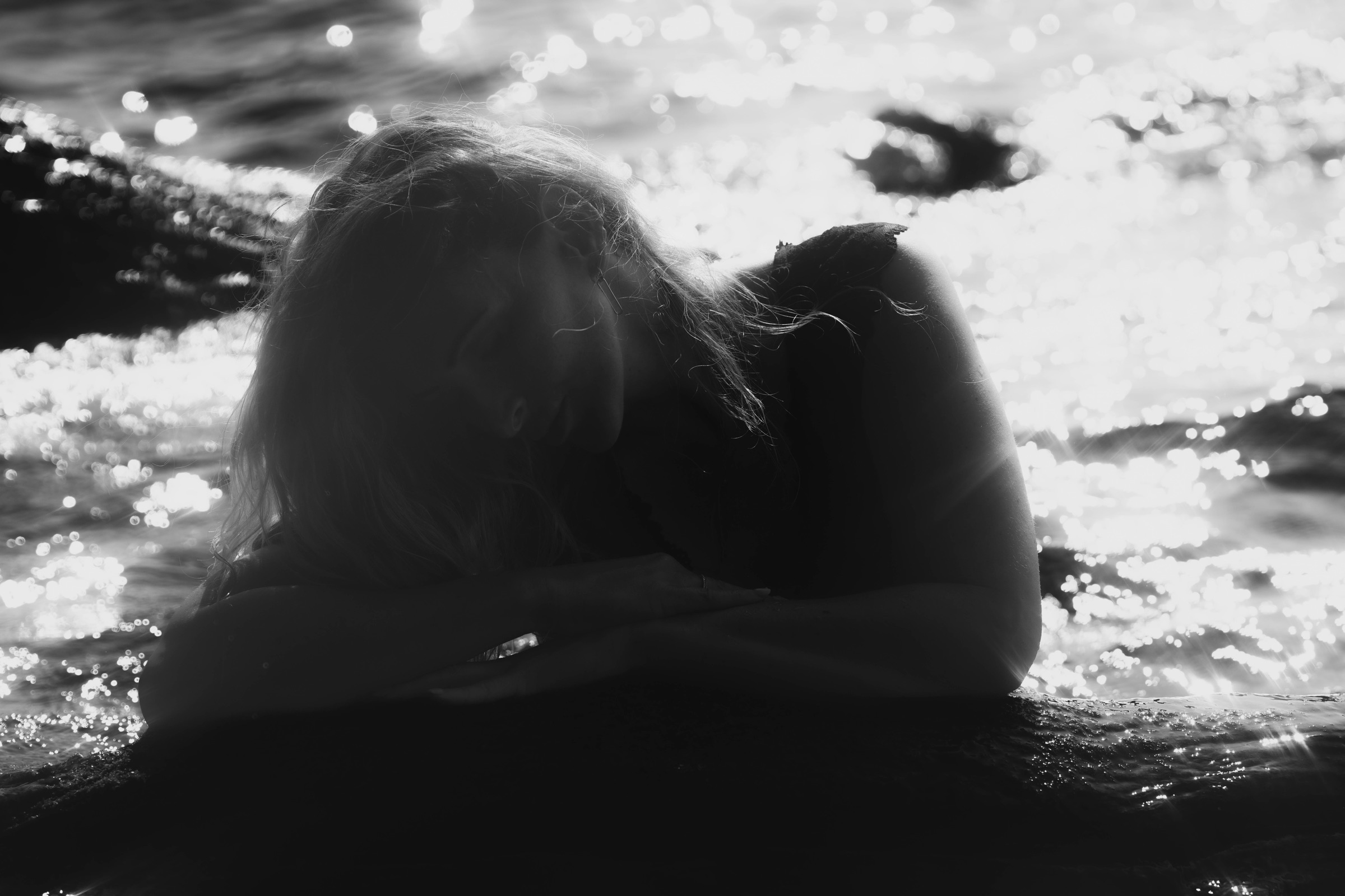 Schwarz-Weiß-Porträt einer Frau im Gegenlicht am Wasser