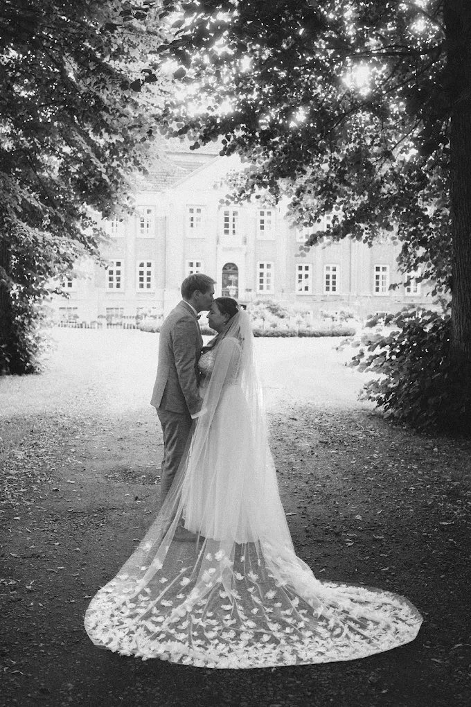 Brautpaar unter Bäumen vor dem Schloss mit langem Schleier